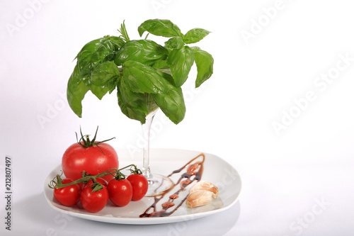 Pomidor czerwony, malinowy i koktajlowy, bazylia, rozmaryn i czosnek na talerzu.