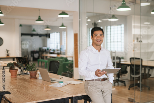 Smiling Asian businessman using a tablet in an office