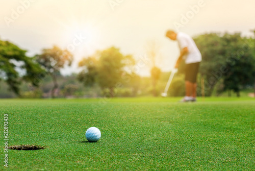 Golfer putting golf ball on green grass course with sunlight in morning time. Sport and recreation playground for golf club concept.