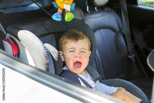 Little baby boy is crying in his car seat not willing to sit in it. Traveling with child and baby safety concept. Little passenger transportation