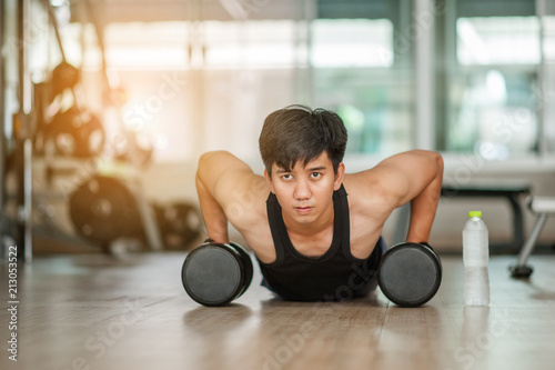 Sport. Handsome man doing push ups exercise with one hand in fitness gym.Fitness instructor at the gym - Control your mind, conquer your body.Handsome muscular man is working out with dumbbells in gym