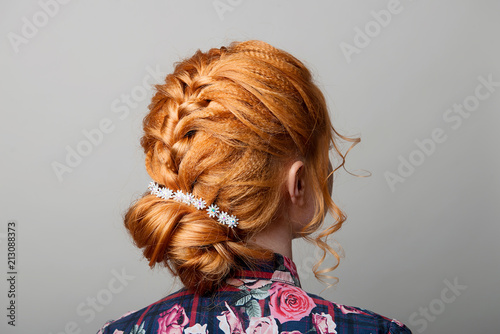 A woman's hairstyle is a low bun on a red-haired girl back view on a gray isolate turning the head to the right.