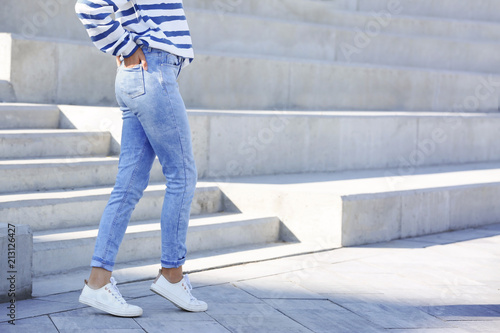 Young hipster woman in stylish jeans standing near stairs outdoors