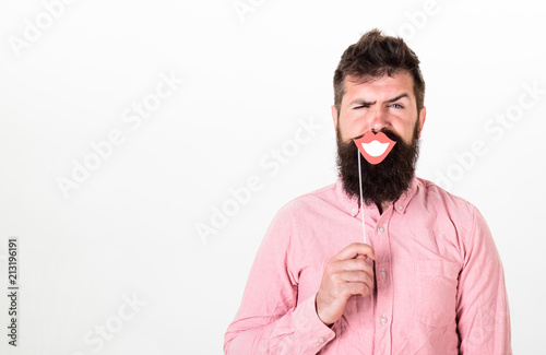 Emotional dissonance concept. Man holding party props smiling lips while his face serious, white background. Hipster with beard and mustache on strict face posing with happy smiling mouth, copy space