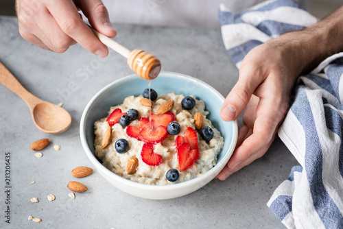 Eating healthy breakfast oatmeal porridge with fresh berries, honey and nuts. Selective focus