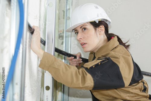 female electrician fitting conduit in wall at construction site