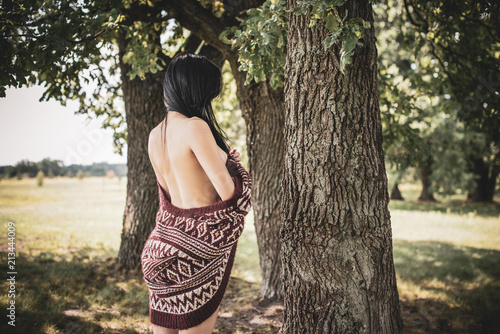 Gypsy girl with long hair posing at nature. A woman with a slim figure and athletic body in knitted sweater, dressed in a sexy kardigan, vintage tones 