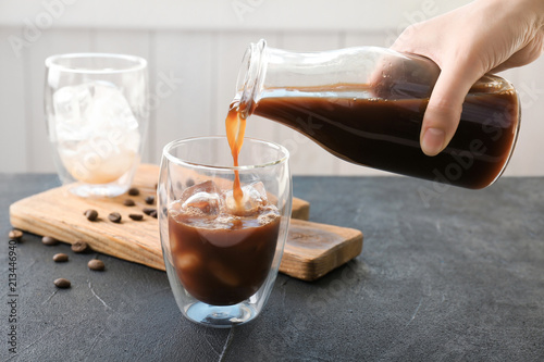 Woman pouring cold brew coffee into glass on table