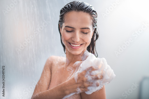 Portrait of happy girl taking shower with gel. She washing with puff