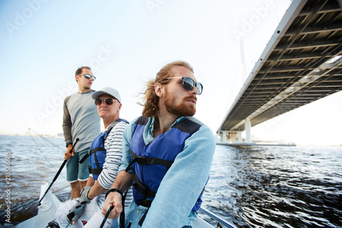 Pensive dreamy men of different ages sailing yacht together and enjoying floating on river, they looking around