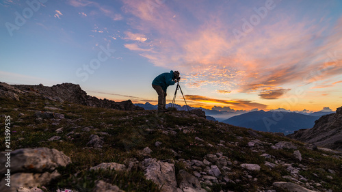 Photographer on mountain top with camera on tripod at sunrise light colorful sky scenis landscape, conquering success leader concept.