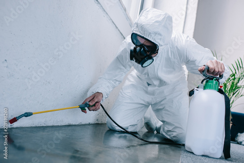 pest control worker spraying pesticides on floor at home