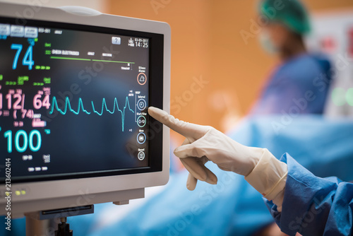 Electrocardiogram in hospital surgery operating emergency room showing patient heart rate with blur team of surgeons background 