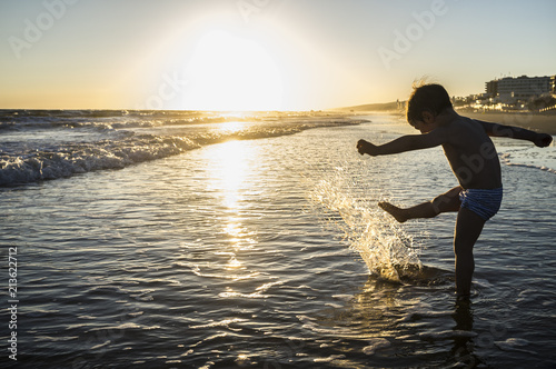 Baby boy playing makes splashes at sunset