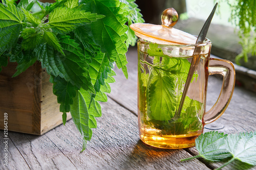 Healthy nettle tea or infusion and nettle herbs on wooden table in retro village house.