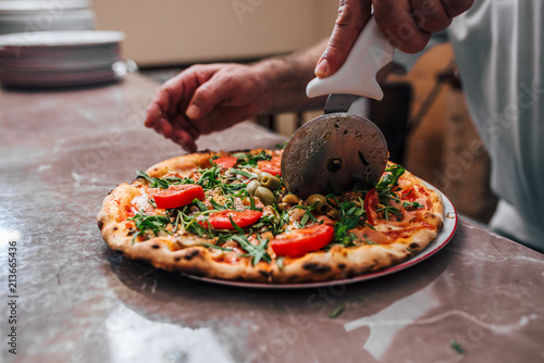 Close-up image of hand of chef baker cutting pizza.