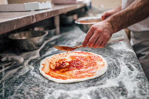 Preparing pizza. Chef's hand adding tomato sauce on pizza dough.