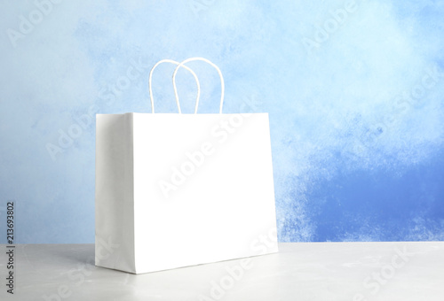 Mockup of paper shopping bag on table against color background