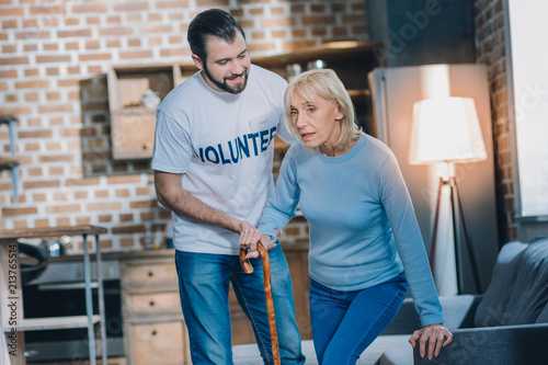 Supportive man. Exuberant young man smiling and helping an old woman while she standing up