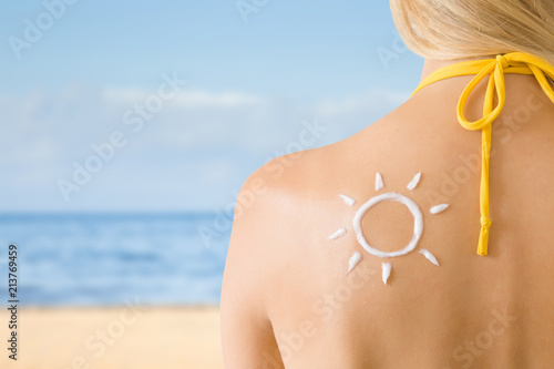 Sun shape created from sunscreen lotion on young woman's back. Skin protection. Hot day. Safety sunbathing concept. Copy space. Empty place for text on beach background.