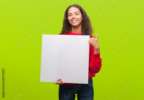 Young hispanic woman holding blank banner happy with big smile doing ok sign, thumb up with fingers, excellent sign