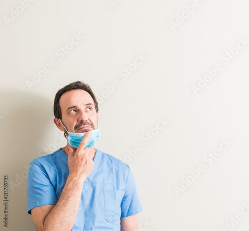 Senior doctor man using mask serious face thinking about question, very confused idea