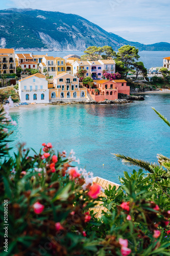 Beautiful colorful southern houses and blue bay of Mediterranean sea with some red flowers on foreground. Assos village in Kefalonia, Greece