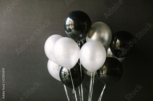 Black and white balloons on a dark black background. Celebration concept / White and black balloons on a dark black background for a holiday, birthday or other holiday. Photo for posters or postcards.