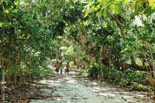 Lavatmangguemu, Pentecost Island / Vanuatu - APR 10 2016: woman walking home with kids on the sea shore path next to their village with an umbrella