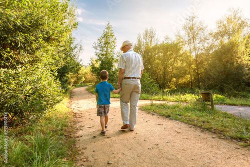 Back view of grandfather with hat and grandchild walking on a nature path