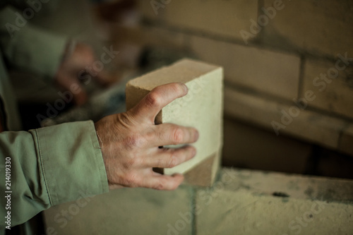 Brickmason's hand holding a brick in front of a brick wall
