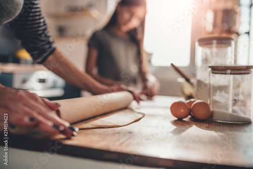 Mother and daughter rolling dough on wooden table