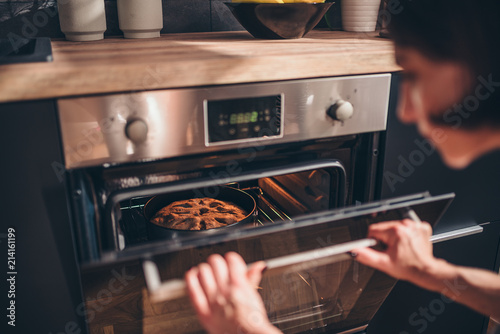 Woman checking apple pie in oven