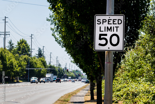 50 mph speed limit sign on post with a road and tree