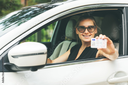 happy young woman showing her driver license through the car window