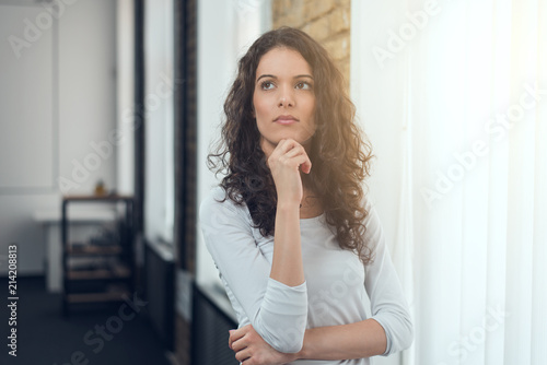 Attractive girl in casual t-shirt squeezing eyes and keeping hand on chin in doubt and suspicion, thinking about something