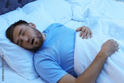 Young man snoring while sleeping in bed at night. Sleep disorder