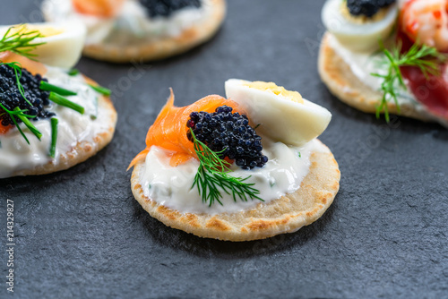 Selection of cocktail blinis with salmon, cured bresaola, crayfish, caviar, quail eggs and sour cream - gourmet party food