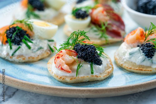 Selection of cocktail blinis with salmon, cured bresaola, crayfish, caviar, quail eggs and sour cream - gourmet party food