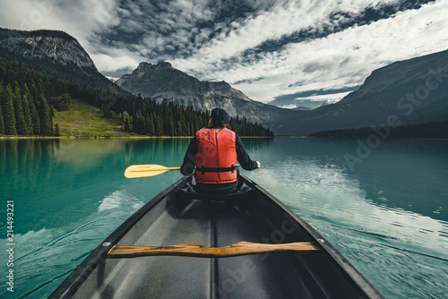 Young Man Canoeing on Emerald Lake in the rocky mountains canada with canoe and life vest with mountains in the background blue water.
