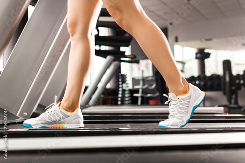 close up girls legs walking at the treadmill in the gym over sunrise. wearing in white orange blue sneakers. Cardio exercise