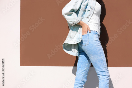 Young hipster woman in stylish jeans and jacket posing near color wall