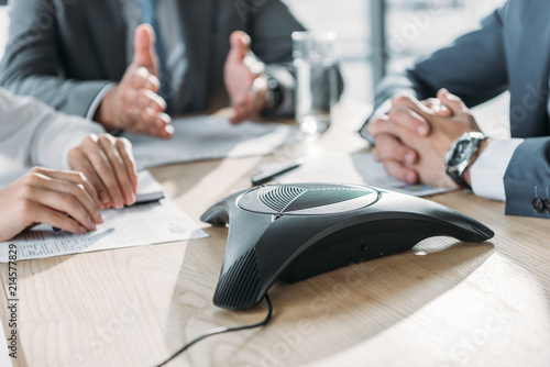 cropped shot of business people having conversation and using speakerphone at modern office