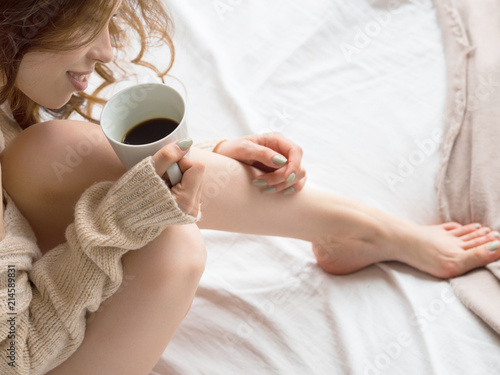Photo of female legs and hands relaxing and drinking coffee in bed early in the morning