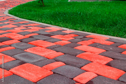 A path from a bright red tile pavers near a juicy green lawn. Bright clinker tiles of different colors for home. For advertising tile manufacturers in the tile catalog.