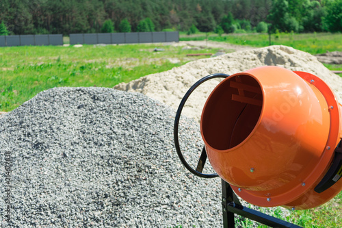 Photo concrete mixer installed on the construction site next to a pile of sand and gravel.