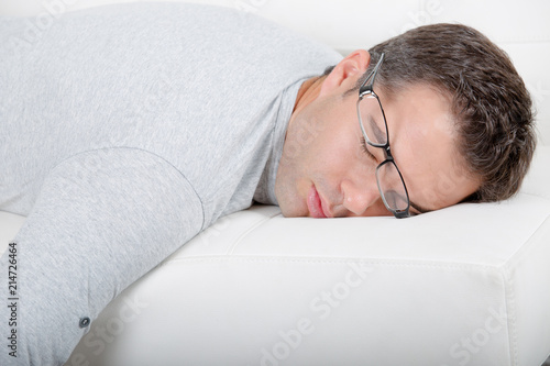 Man asleep on sofa, glasses being pushed off of his face
