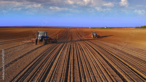 Farmers in tractors seeding, sowing agricultural crops in field at sunset