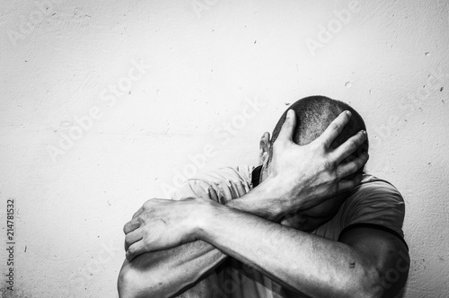 Homeless man drug and alcohol addict sitting alone and depressed on the street feeling anxious and lonely, social documentary concept black and white