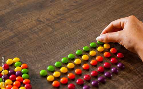 woman's hand collects even row of colorful candies on a wooden background